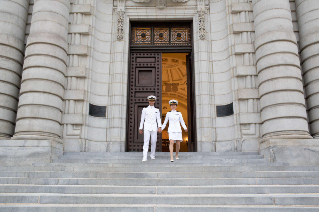 Naval Academy couple walking down stairs of Bancroft Hall in white uniforms.