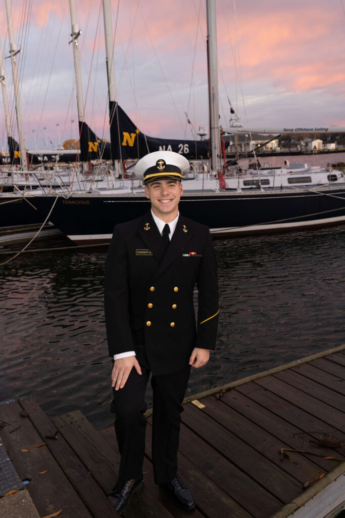 Naval officer in dress blues at sunrise with boats on pier at USNA in Annapolis Maryland.